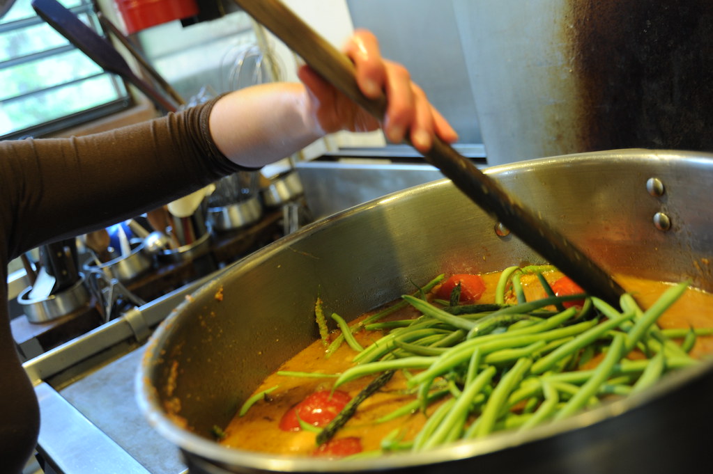 Person stirring a large pot of fresh green beans and vegetables while batch cooking in a home kitchen