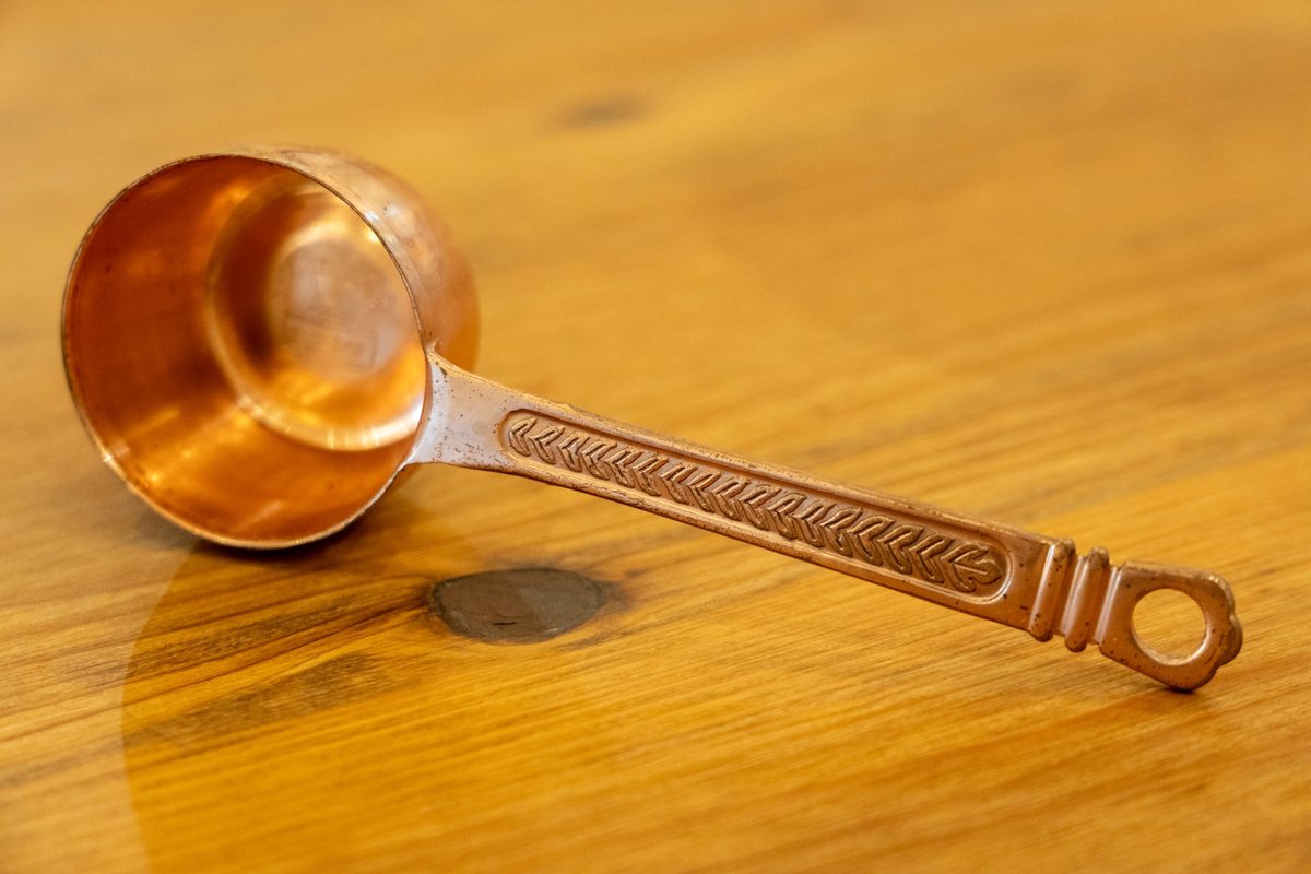 A bronze measuring spoon resting on a clean wooden tabletop