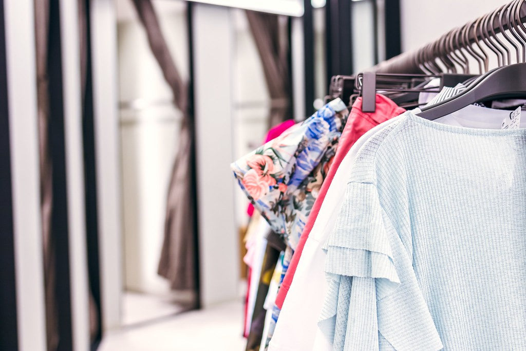 Rack of shirts and colorful clothing beside a store fitting-room area