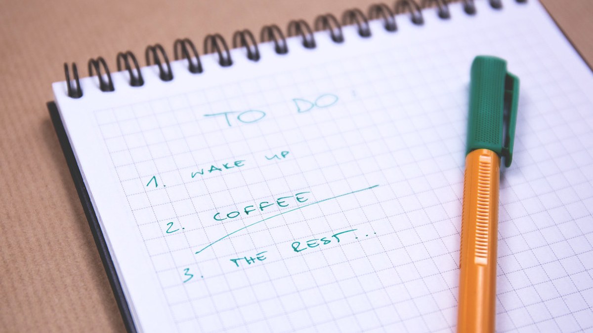 A handwritten to-do list in a spiral notebook with a pen on a wooden desk
