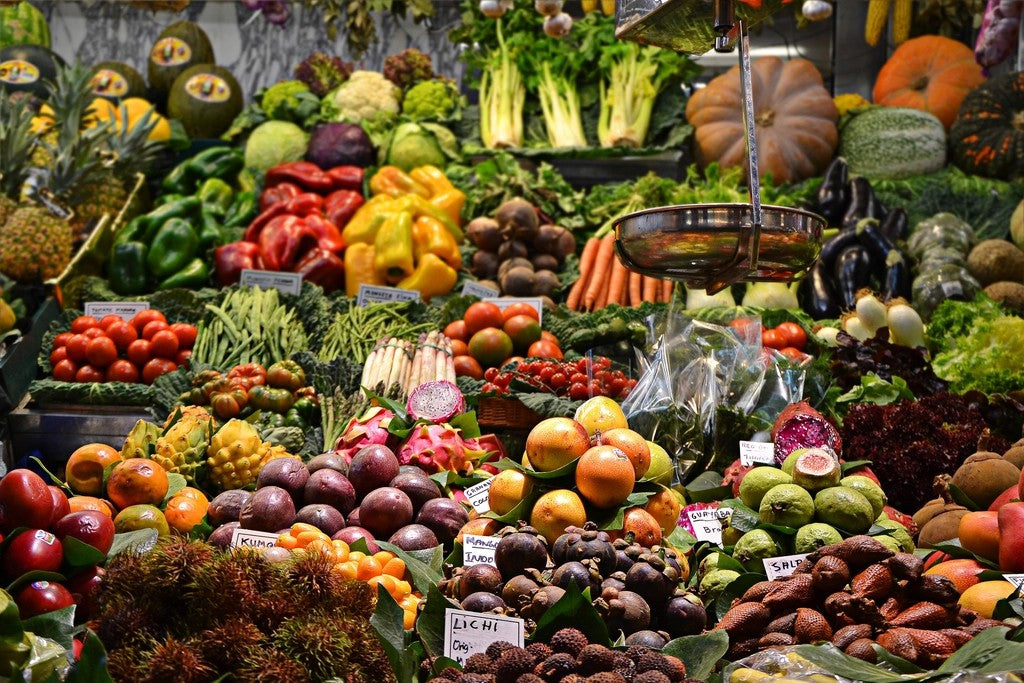 Colorful fruits and vegetables displayed around a hanging scale at a market stall