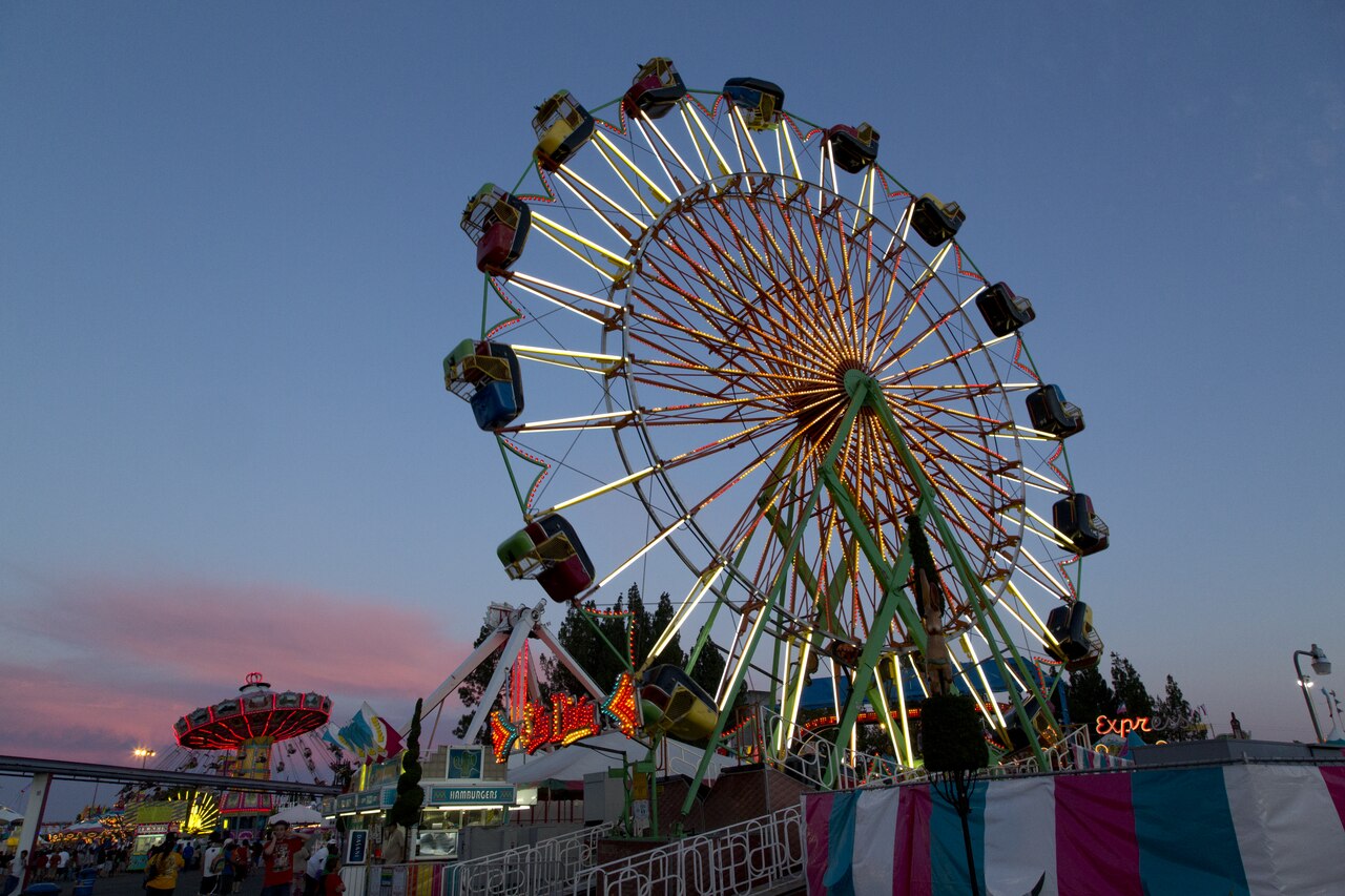 Illuminated Ferris wheel and midway at a county fair under a blue and pink evening sky