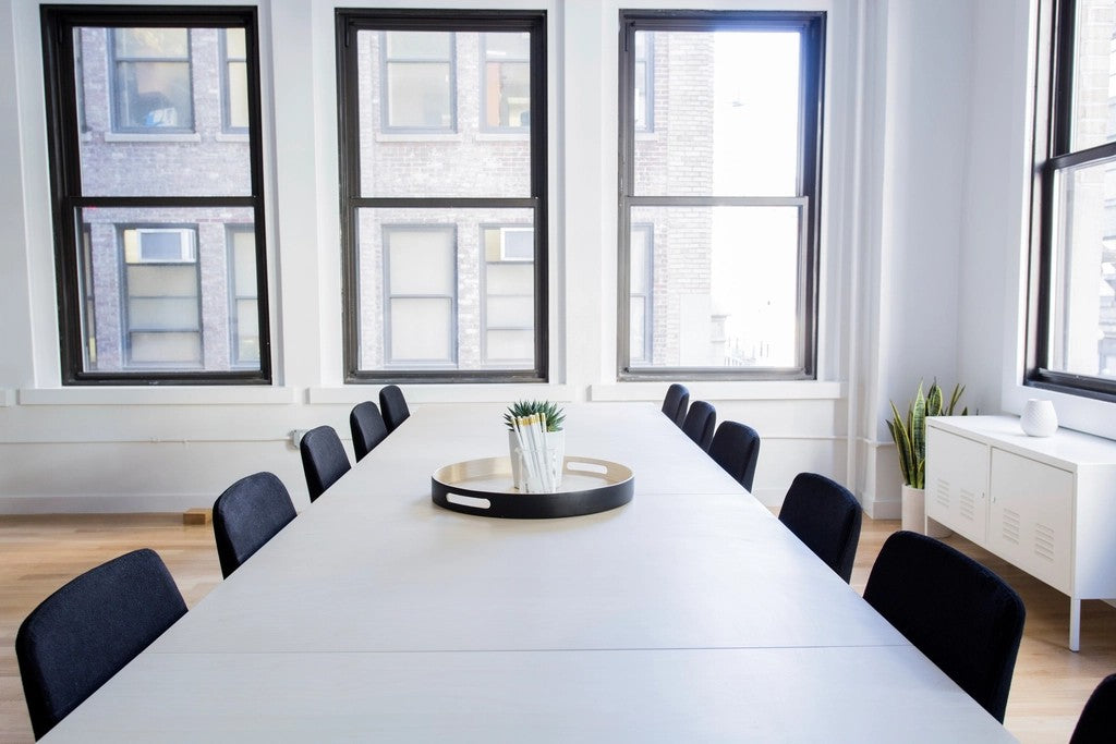 Bright empty shared workspace with a long table, chairs, windows, and a clear path around the room