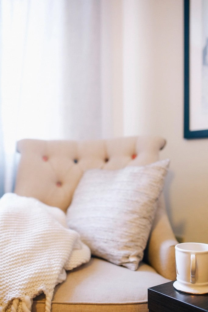 Cozy armchair with a knitted blanket, cushions, and a mug in soft daylight