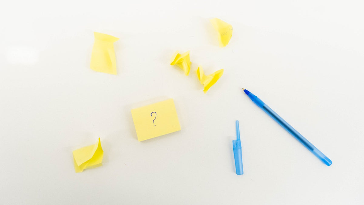 Yellow sticky notes and a blue pen arranged around a question mark for a two-option planning exercise