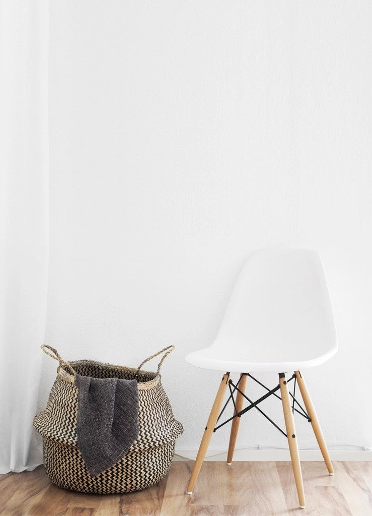 Woven laundry basket beside a chair in a bright, uncluttered room