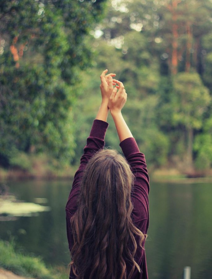 A person in a cozy sweater gently stretching outdoors in a quiet natural setting