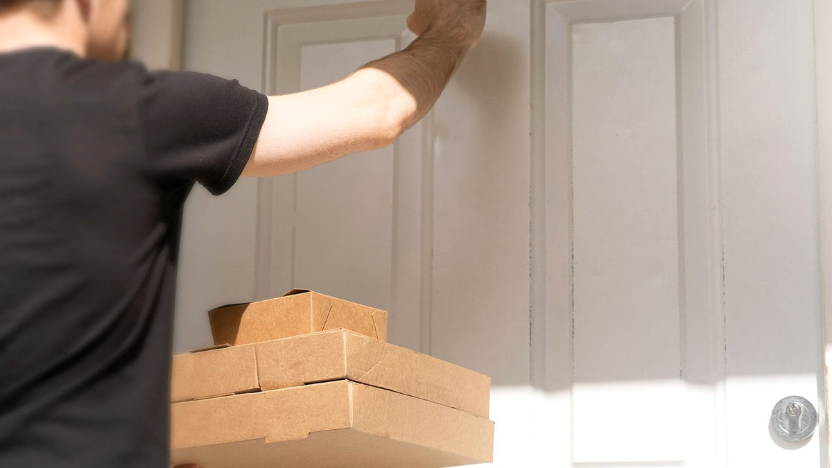 Delivery worker holding plain cardboard packages while knocking on a white front door