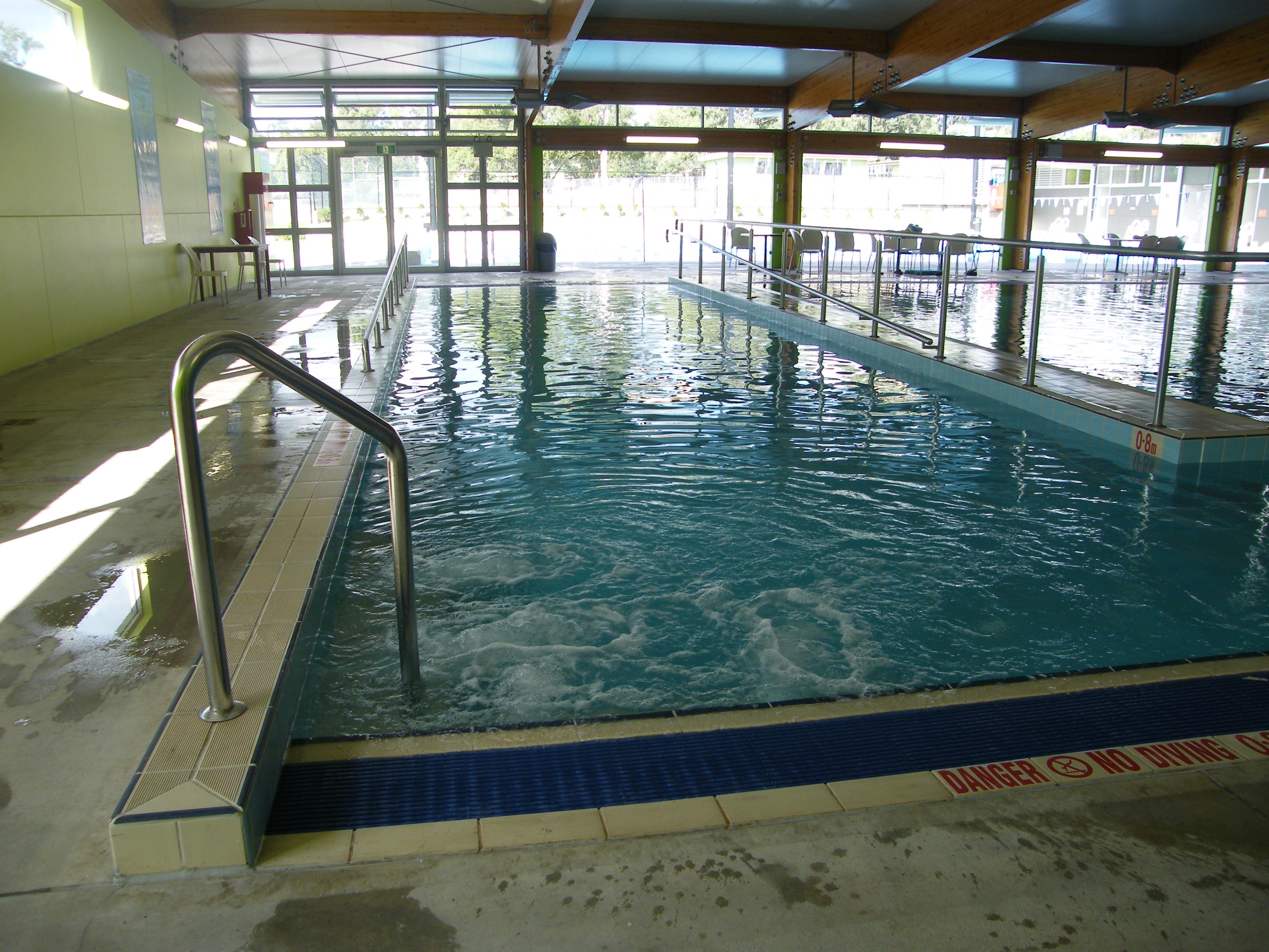 Empty indoor community pool with handrails and a broad access ramp beside the water