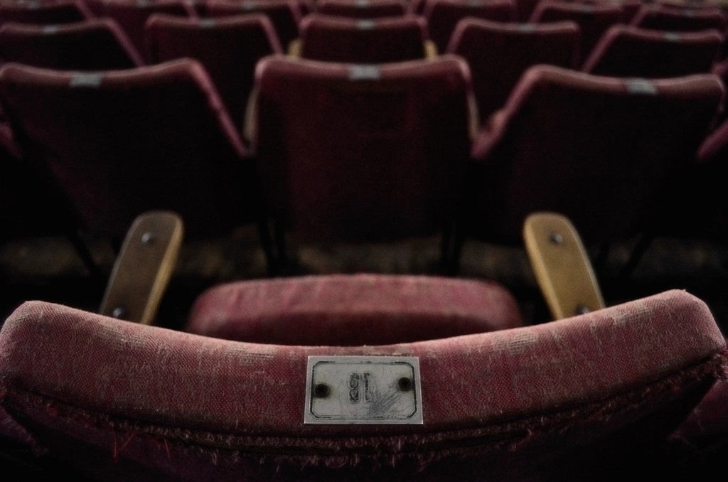 Rows of red movie theater seats with an aisle-side seat in focus
