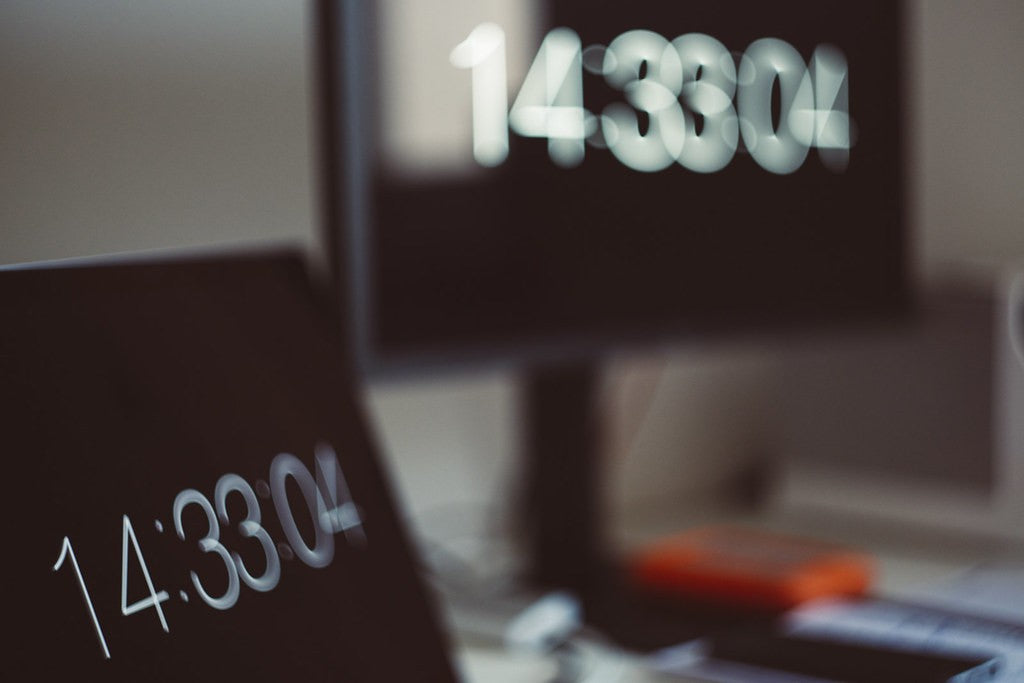 Soft-focus office workstation with an empty chair and digital clock reflections