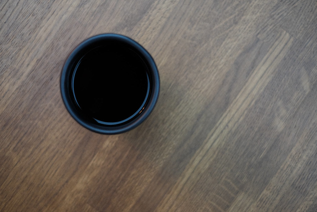A dark mug of coffee viewed from above resting on a wooden table