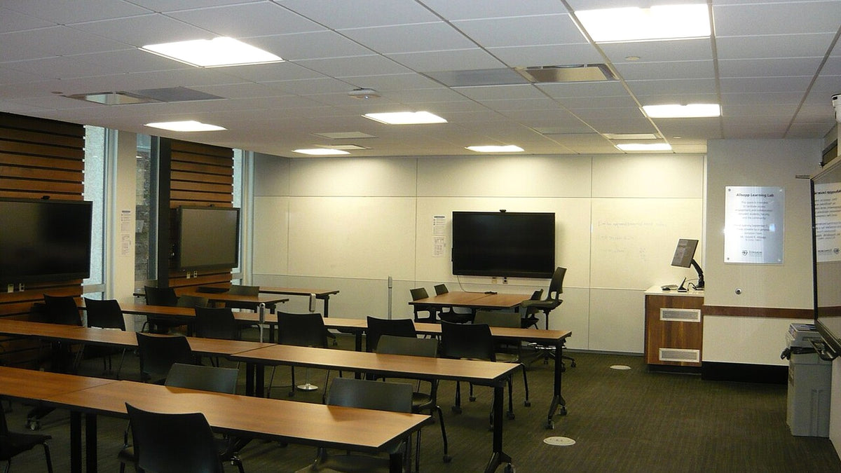 Empty public lecture room with rows of tables, chairs, open walkways, and a presentation lectern