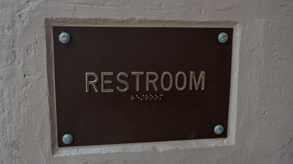 A close view of a restroom sign with braille, representing accessible bathroom planning with IBD