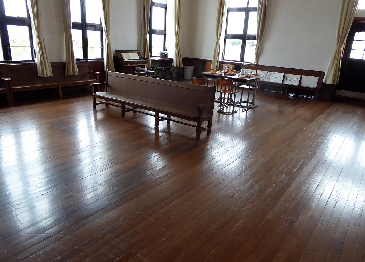 Quiet school meeting room with wooden benches, desks, and daylight through tall windows