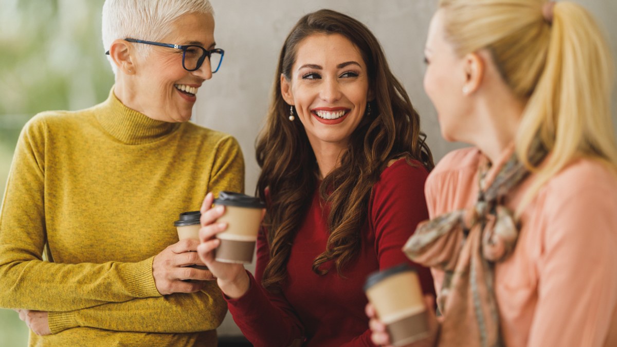 Three friends smiling and talking together over coffee