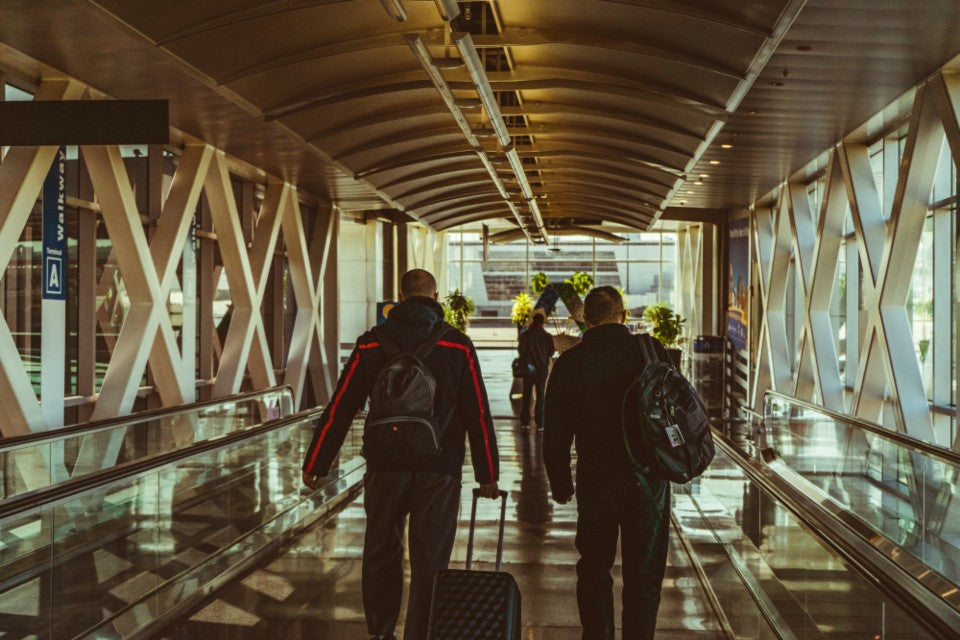 Travelers carrying bags and rolling luggage through a warm airport terminal