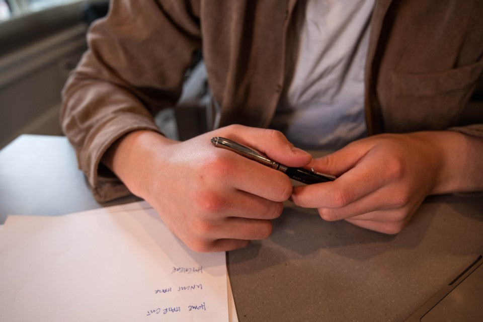 Adult holding a pen over a paper note at a desk, ready to mark a clear next step