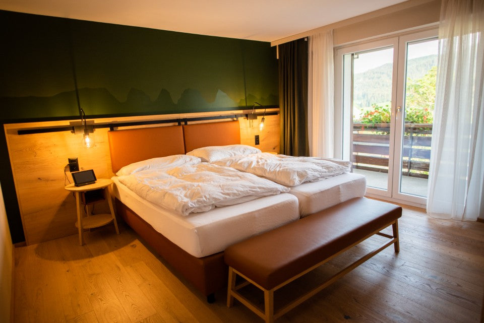 Warm hotel room with separate beds, a bench, privacy curtains, and a clear floor