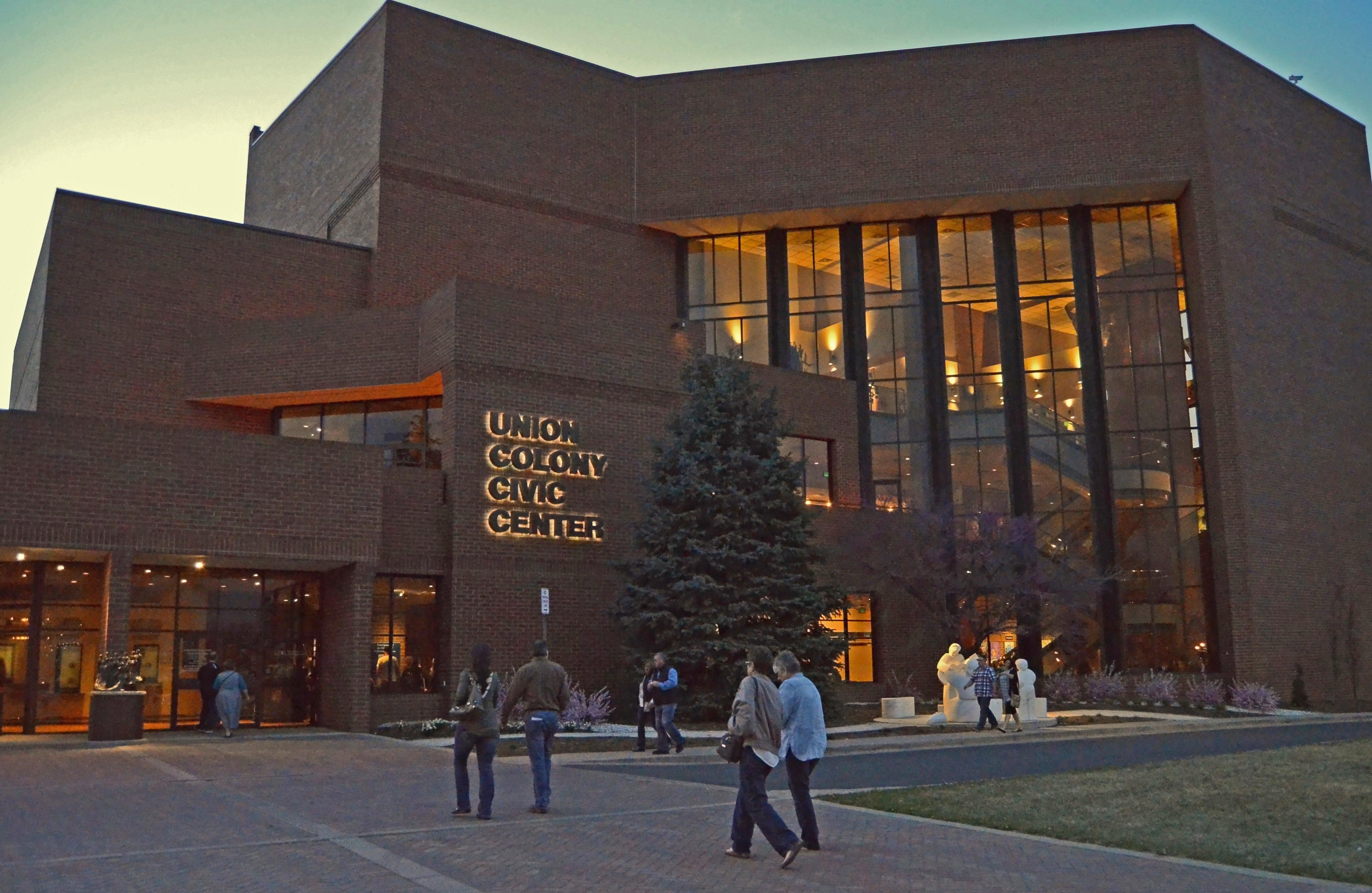 People arriving outside a warmly lit performing arts venue at dusk
